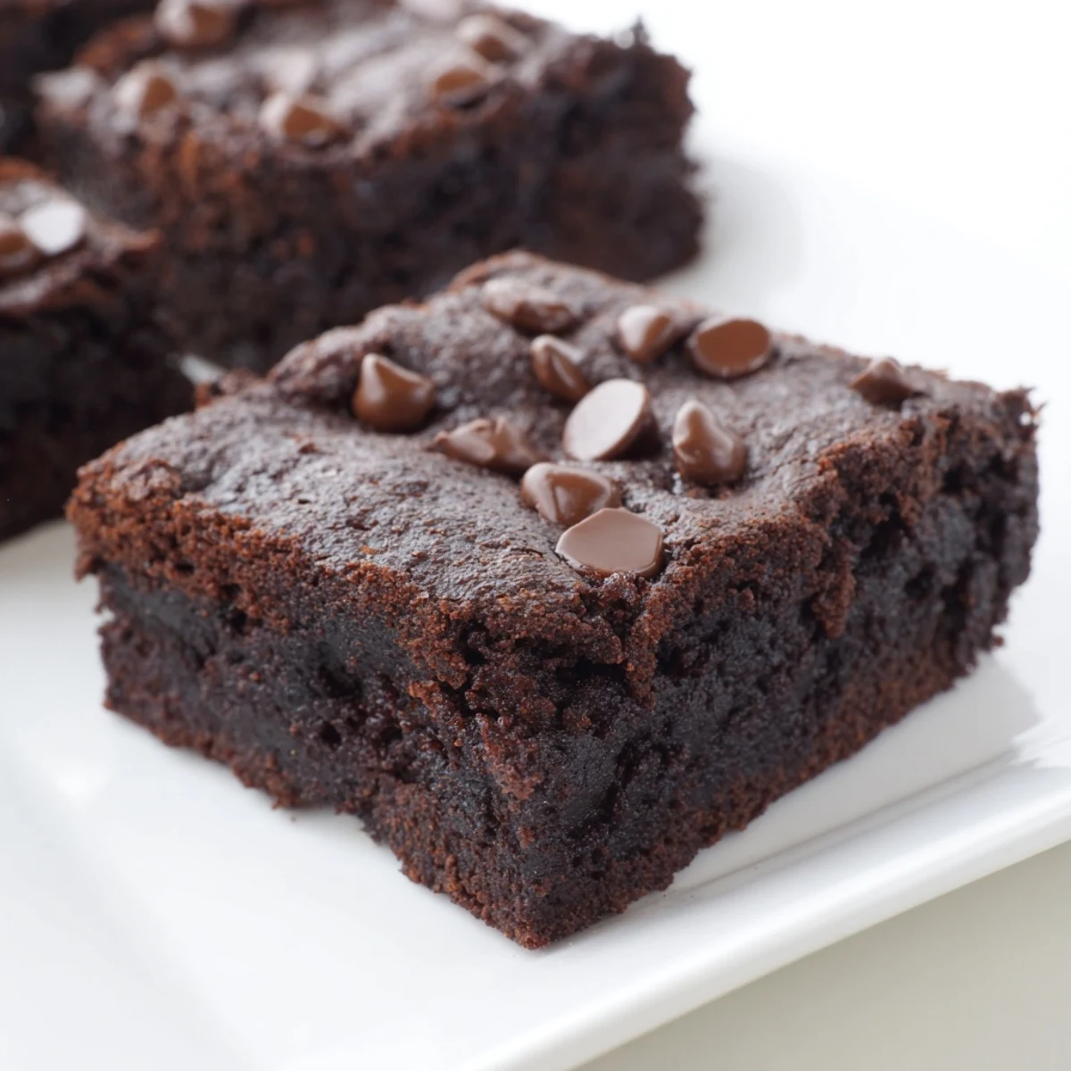 Fudgy black bean brownies, warm from the oven, with a glistening chocolate chip topping, ready to serve.