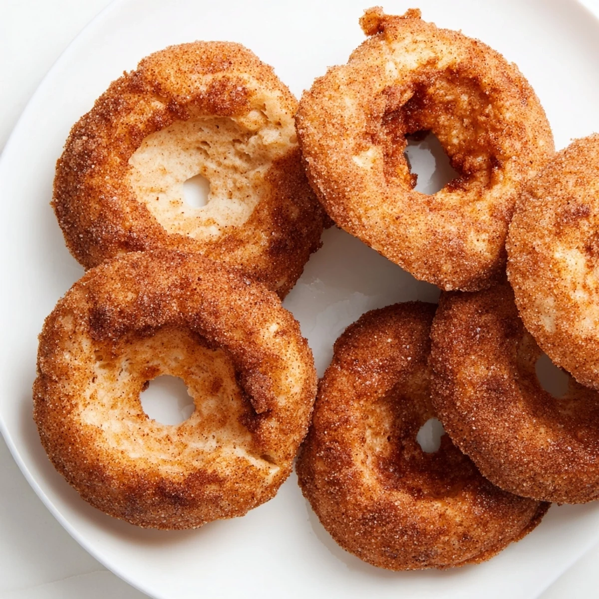 Golden Air Fryer Cinnamon Sugar Donuts coated in sugary glaze, served warm on a white ceramic plate.