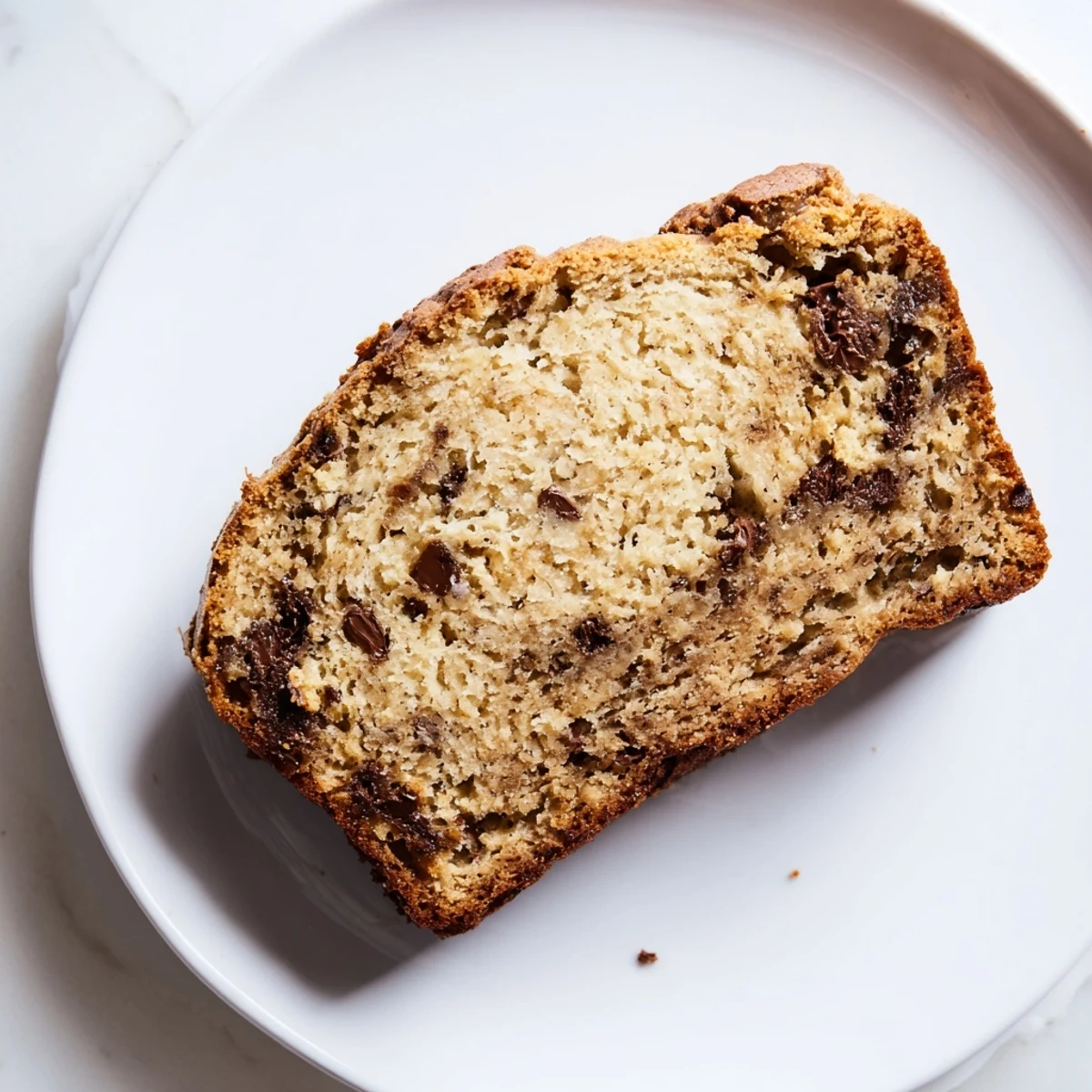 A freshly baked loaf of moist banana bread with chocolate chips, served warm with melting butter on a rustic cutting board.  