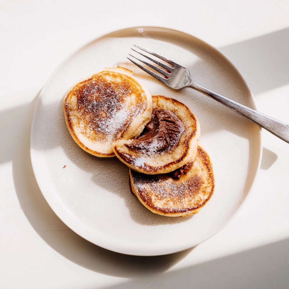 Fluffy golden Nutella Stuffed Pancakes served warm with powdered sugar dusting.