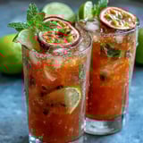 Chilled glasses brim with vibrant pink tropical sips of the DIY Iced Guava Passionfruit Drink, garnished with fresh mint and lime.