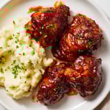 Juicy honey BBQ chicken thighs, perfectly glazed, paired with creamy garlic mashed potatoes, a real warm plate.