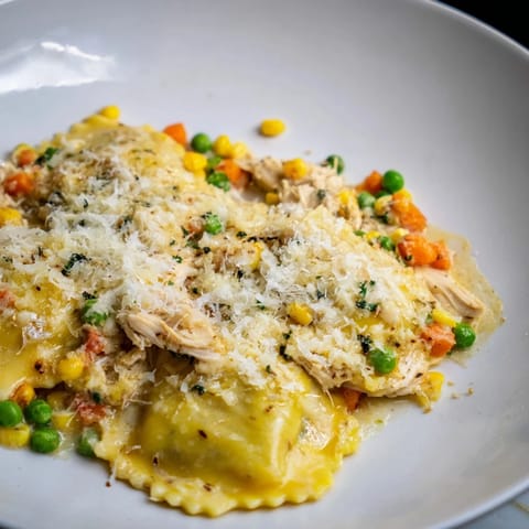A close-up of a Chicken Pot Pie Ravioli Bake, showing creamy filling and golden, melted cheese on top.