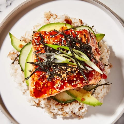 Tender Emily Mariko-Inspired Sticky Orange Gochujang Salmon Bowl beside fluffy rice, with sesame seeds and nori strips.