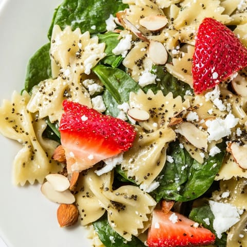 A vibrant bowl of Spring Spinach Strawberry Pasta Salad with feta, toasted almonds, and herbs, perfect for a sunny picnic or potluck.