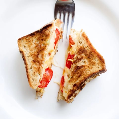 A close-up of a pepper jack and tomato grilled cheese sandwich shows melted cheese oozing from crispy, golden-buttered bread.