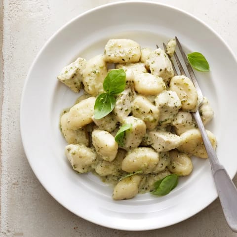 Golden-brown pan-crisped gnocchi and tender chicken cubes coated in a vibrant green basil pesto cream sauce, served in a rustic skillet.  