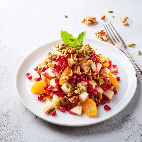 A vibrant bowl of pomegranate and walnut salad garnished with fresh mint and sprinkled seeds, perfect for winter gatherings.  