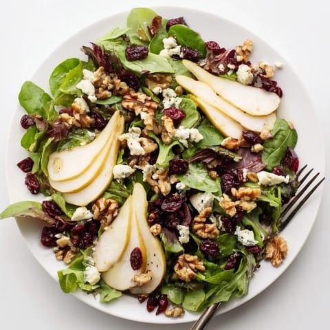 Pear Gorgonzola Salad arranged on a white plate, featuring juicy pear slices, blue cheese crumbles, toasted nuts, and greens for a light lunch.