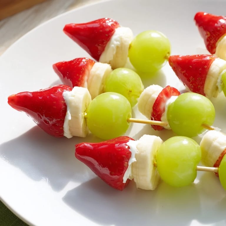 A vibrant photo shows Elf Hat Strawberry Skewers, a festive healthy snack idea with fresh grapes.