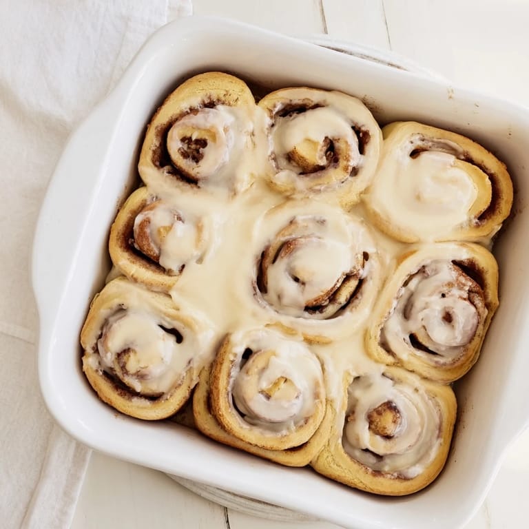 Golden-brown Pillow Soft Cinnamon Rolls topped with luscious cream cheese frosting on a baking sheet.  