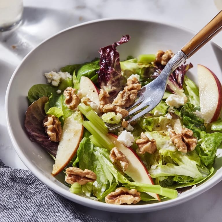 Vibrant bowl of Apple and Walnut Salad featuring shiny green apple slices, chopped walnuts, and greens glistening with a sweet and tangy dressing.