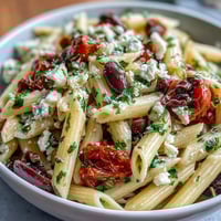 A colorful bowl of Greek pasta salad with olives and feta, tossed with crisp vegetables and a tangy Mediterranean dressing.