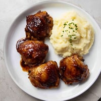 Golden-brown honey BBQ chicken thighs glistening, served with fluffy garlic mashed potatoes for dinner.